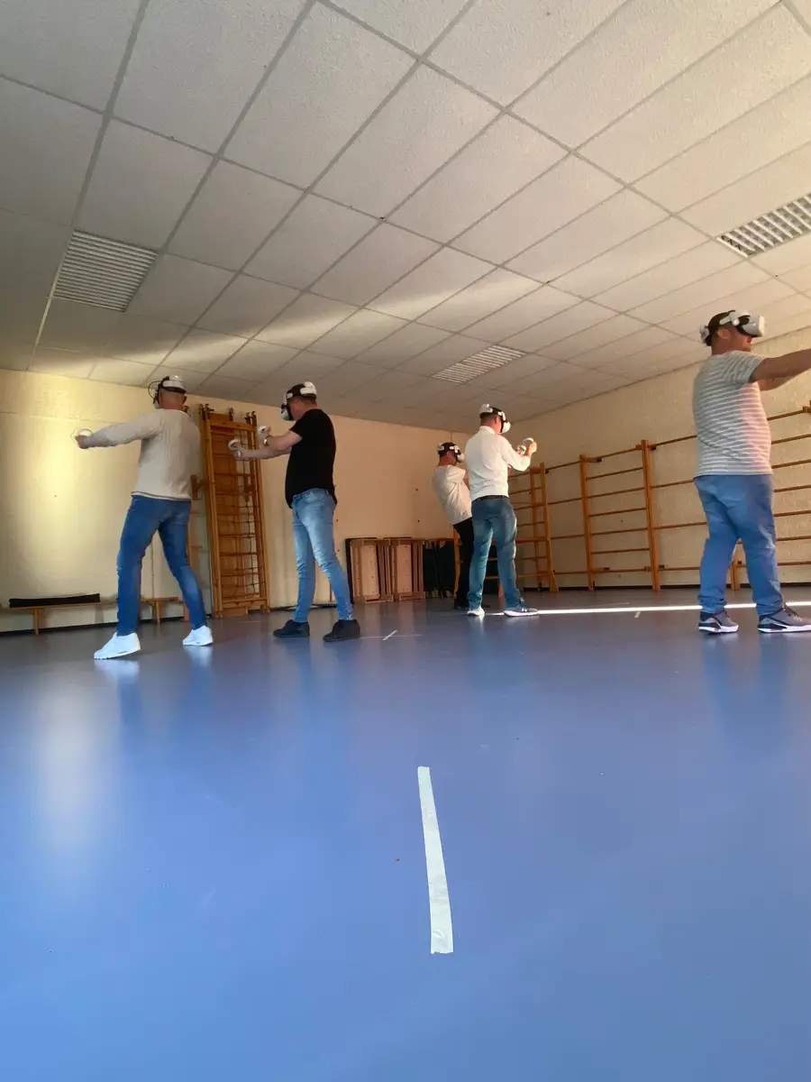 Vier spelers met VR-bril verspreid door een gymzaal met wandrekken