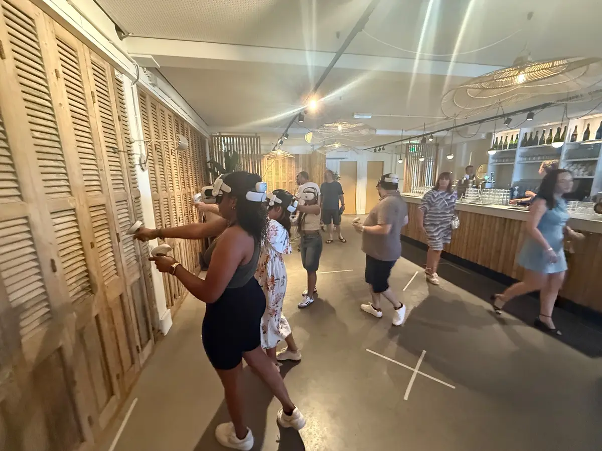 Spelers met VR-brillen bewegen door een lange zaal met een bar
