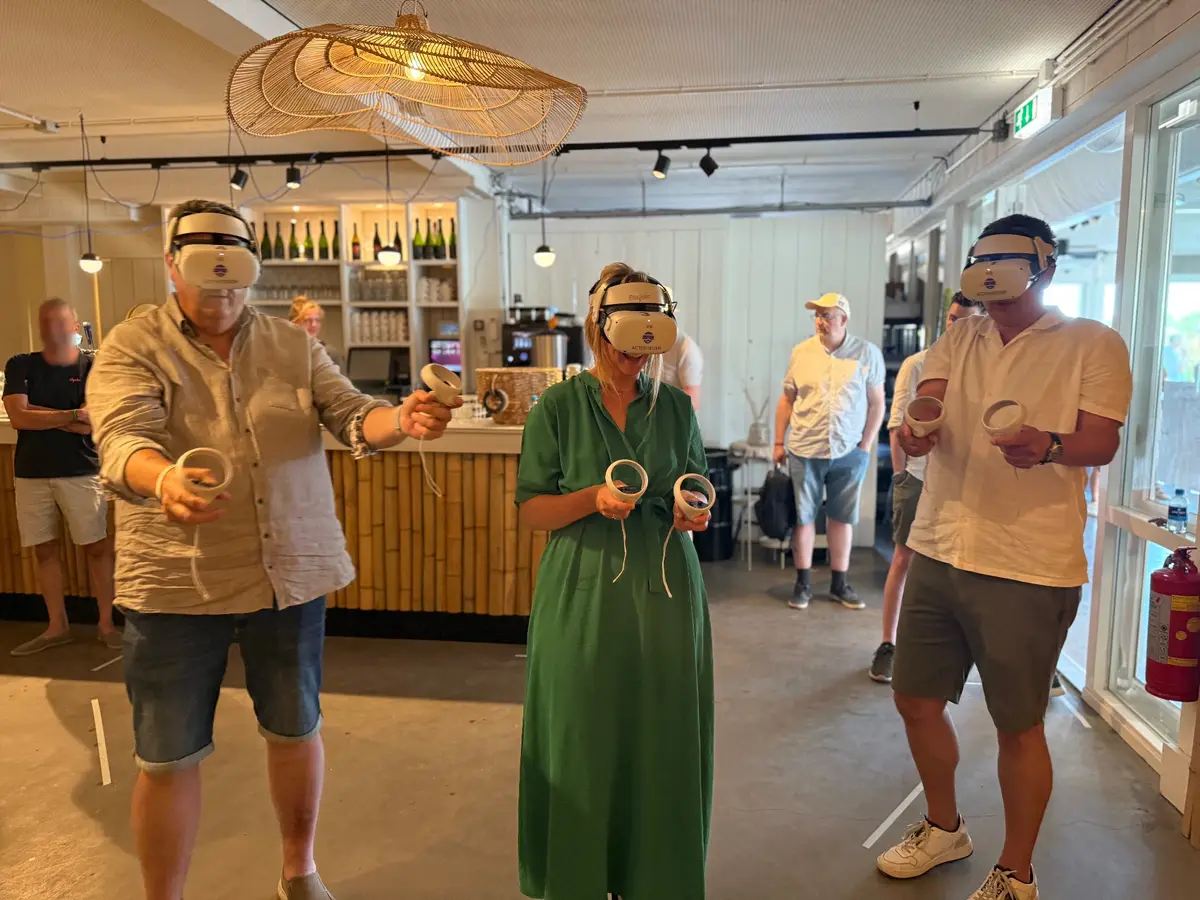 Drie spelers met VR-bril in een horecazaal, met de bar op de achtergrond