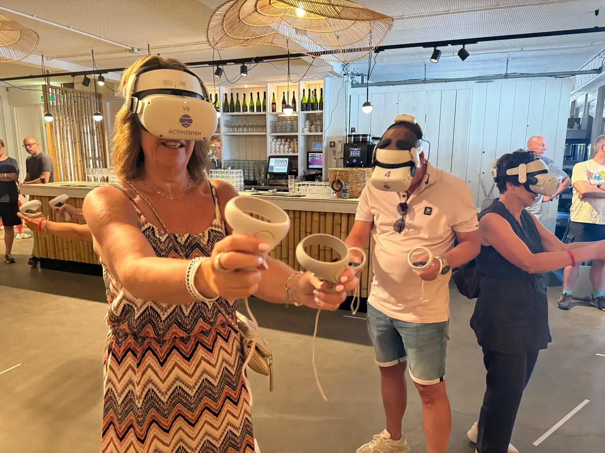 Speelster met VR-bril richt haar controllers naar voren, naast twee medespelers