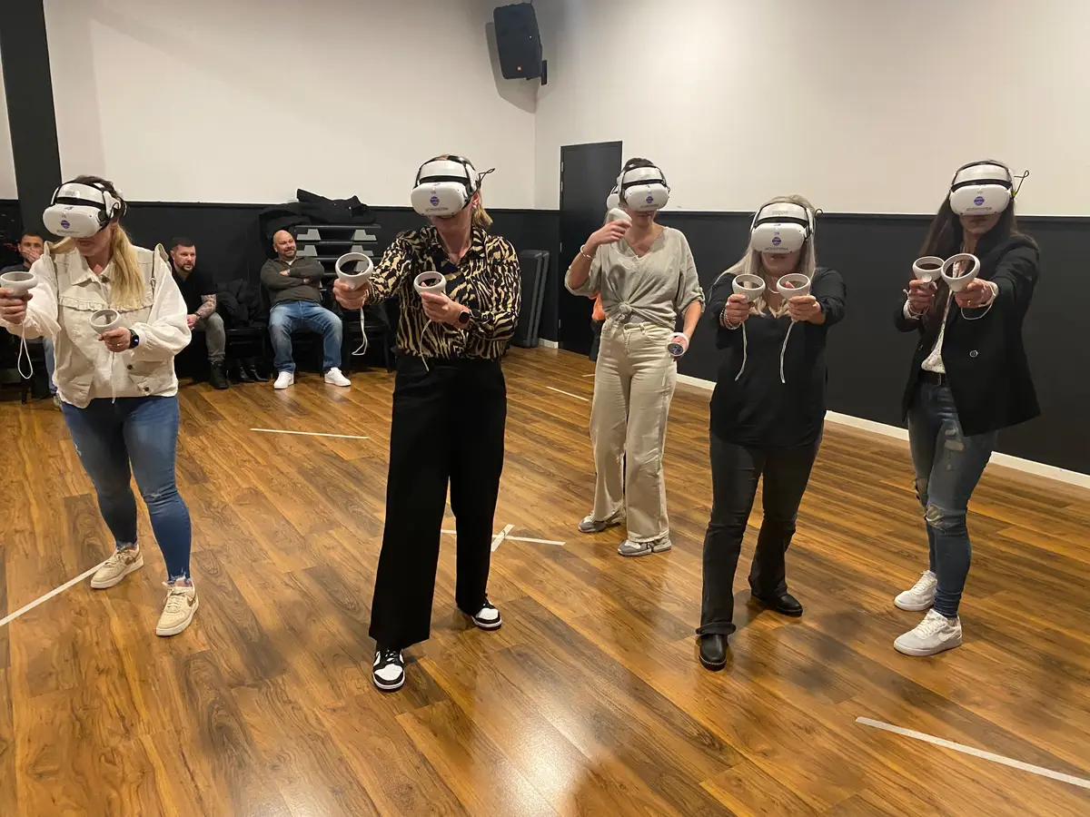 Zes spelers met VR-brillen naast elkaar in een zaal met houten vloer